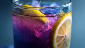 Close-up van een glas butterfly pea iced tea met citroenschijfjes en paarse-blauwe kleurverloop.